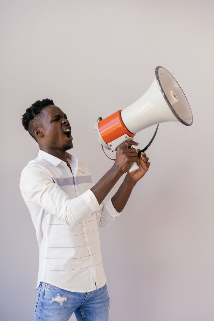 Man shouting into a megaphone during a studio shoot, expressing emotion.